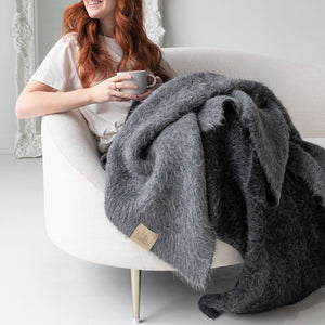 Woman holding coffee cup with BIG LOViE Suri baby alpaca blanket in black and dark gray on her lap.