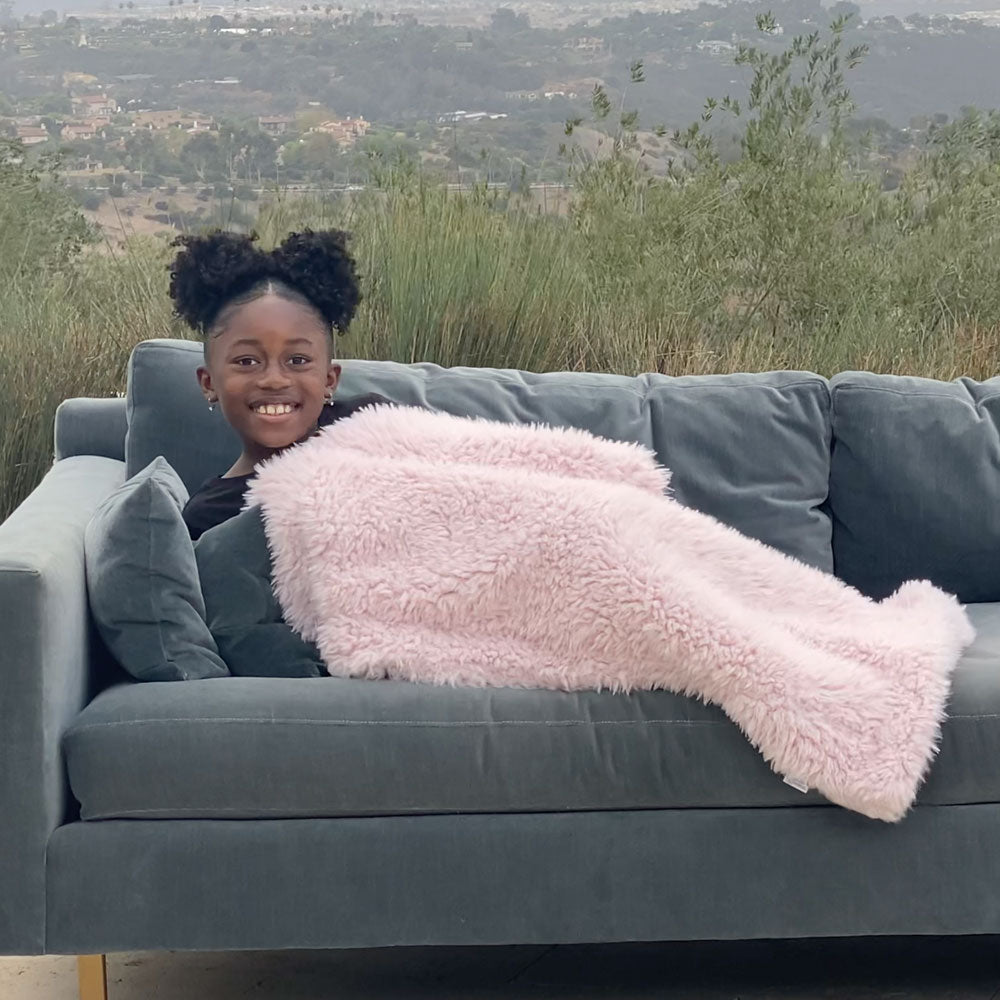 Young girl laying on couch covered with BIG LOViE Little Guardian Angel Blanket in dusty pink.