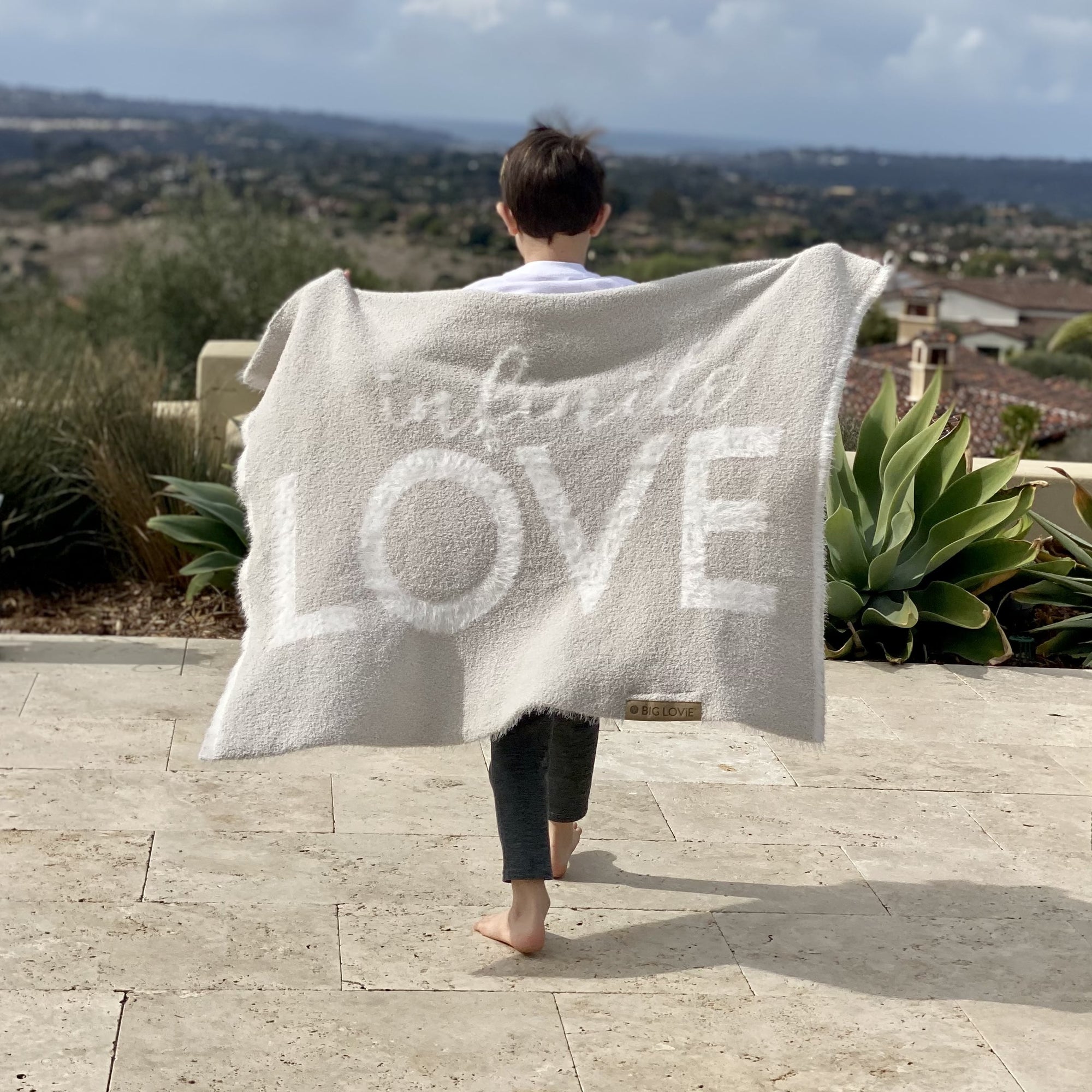 Small child wearing BIG LOViE Dream Collection Little Infinite Love blanket as a cape.
