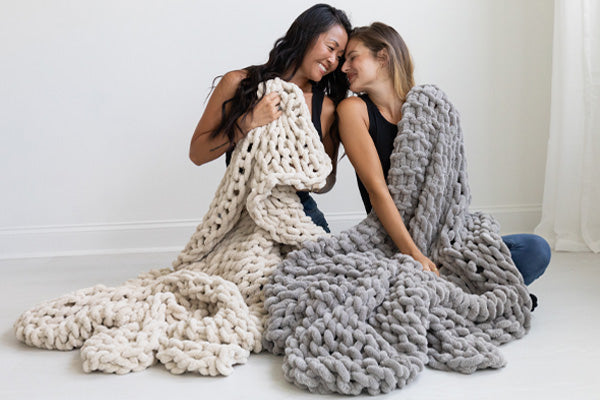 BIG LOViE Infinite Chunky Knit Minky Big Blankets in Sand and Mist, wrapped around two friends.