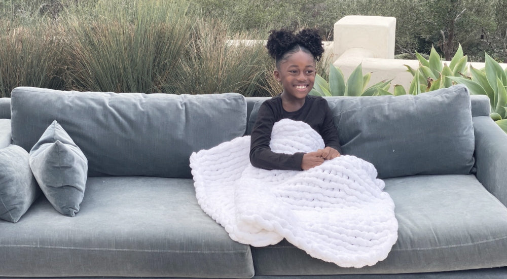 BIG LOViE Infinite Chunky Knit Blanket on little girl smiling on outdoor sofa