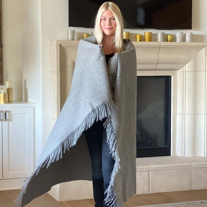 Woman wrapped in BIG LOViE Soul KJ 100% Alpaca Eco blanket in Gray standing in front of fireplace..