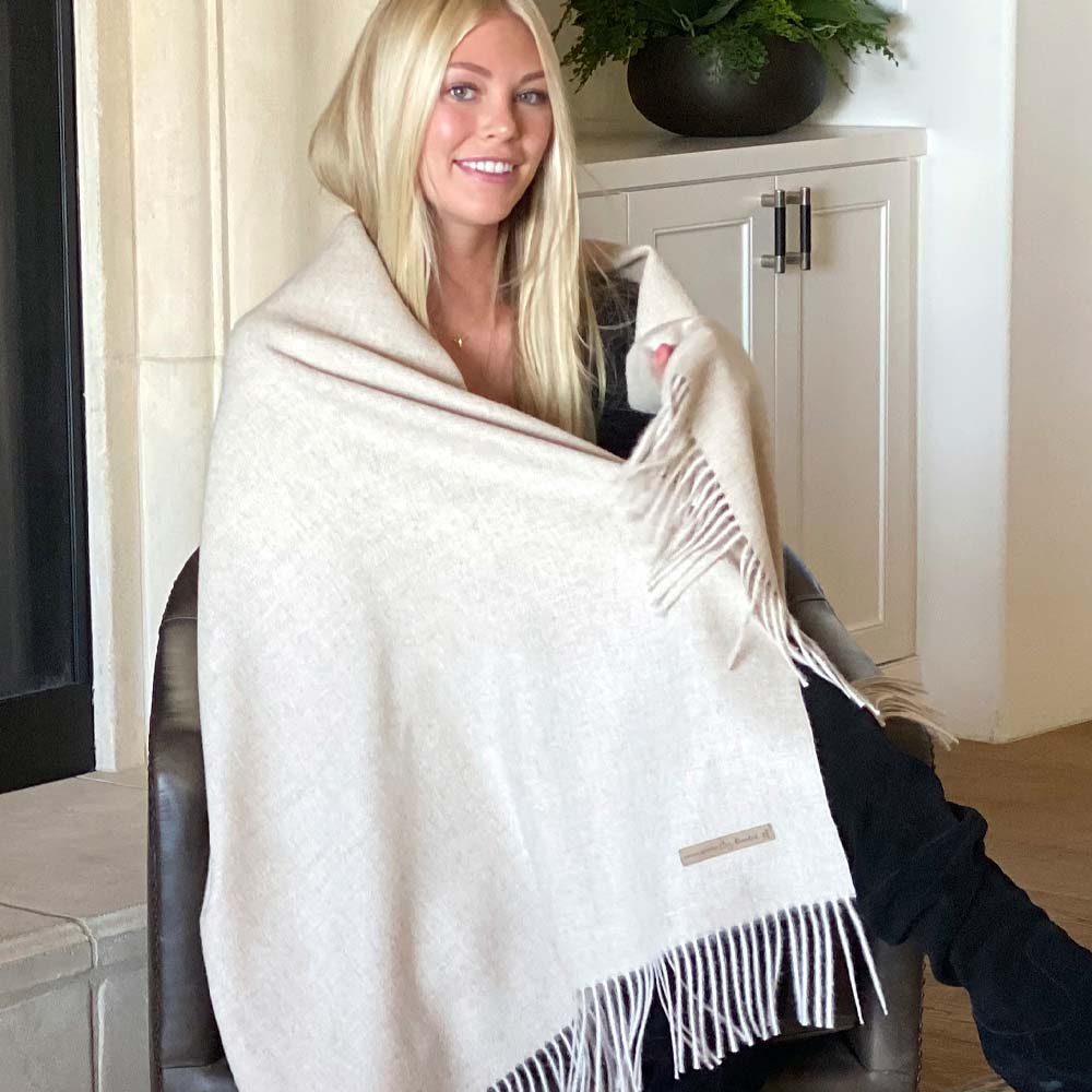 Smiling woman wrapped in BIG LOViE Soul KJ 100% Alpaca Eco blanket in Taupe sitting in chair.