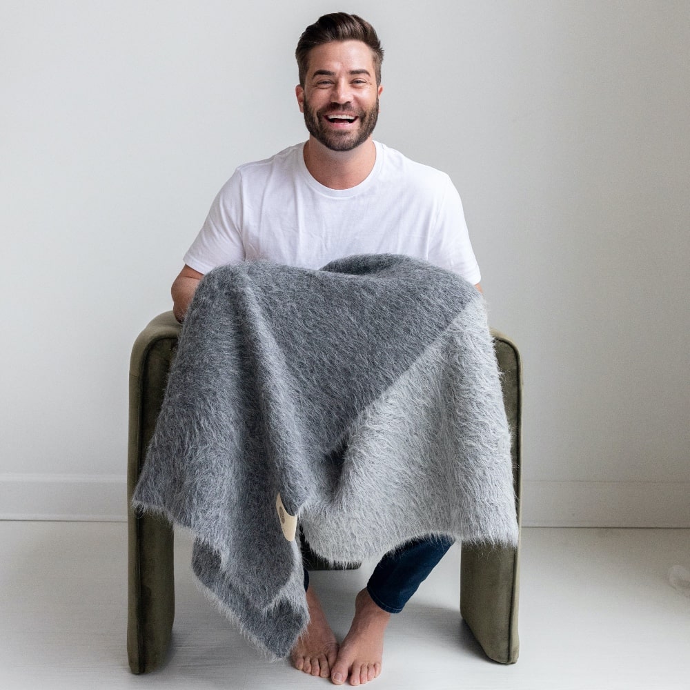 Laughing man holding BIG LOViE Suri baby alpaca blanket in dark gray and light gray.