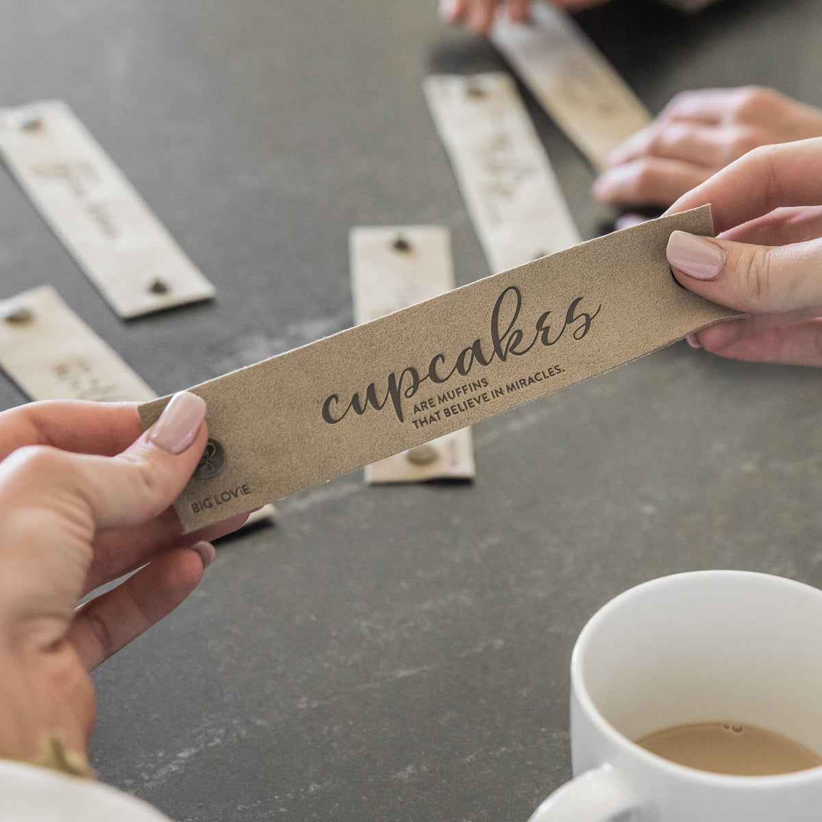 Woman with pink nails holding up LoveSnap, coffee on table