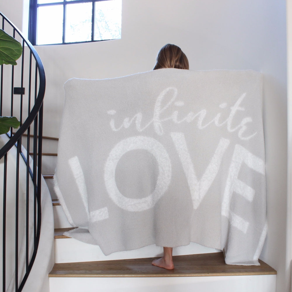 Young girl standing on stairs, arms spread out holding the Love Blanket from the Dream Collection, micro-chenille and feather yarn, light grey blanket 