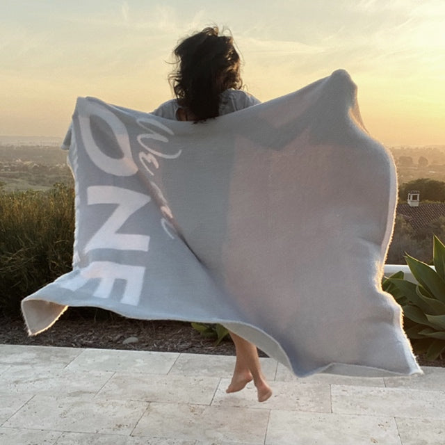 Woman jumping outside at sunset, wrapped in her One Blanket from the Dream Collection, micro-chenille and feather yarn