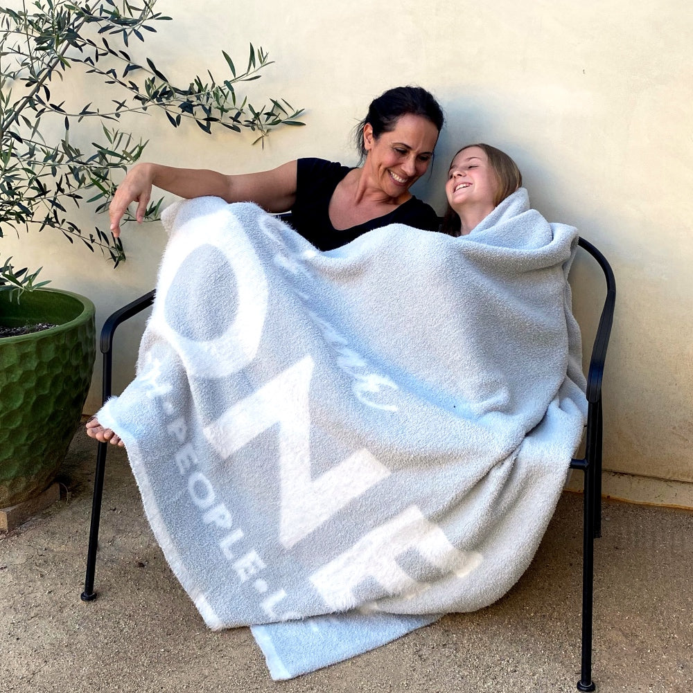 Mother and daughter sitting on chair together, smiling, in One Blanket from Dream Collection, micro-chenille and feather yarn