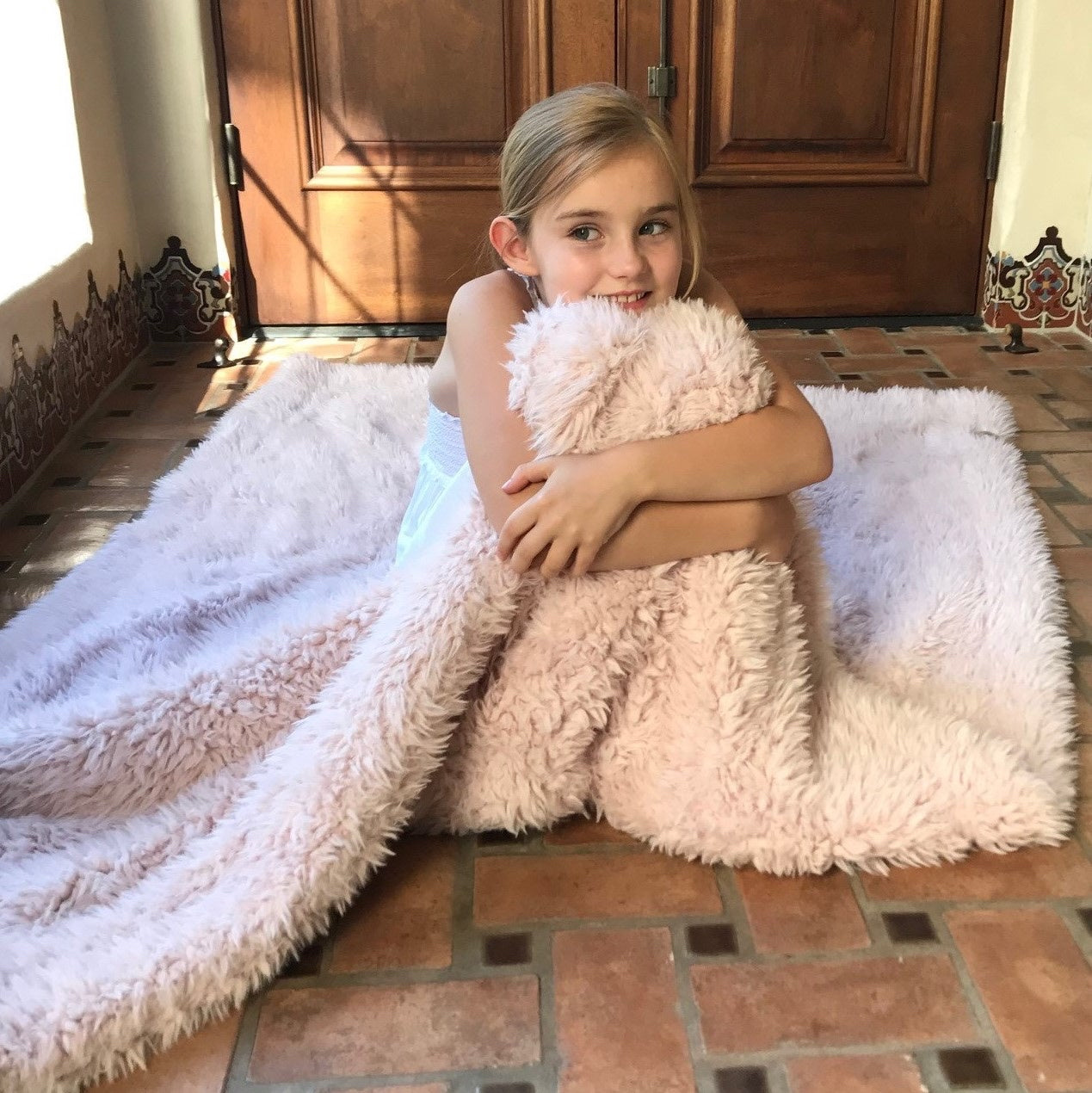 A little girl sitting on the floor, cuddled in her big guardian angel blanket, dusty pink, llama fabric