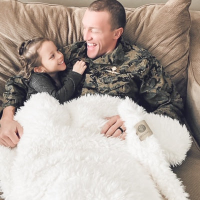 Military dad and daughter snuggled in their BIG LOViE Big Guardian Angel Blanket in Whisper White, plush llama fabric 