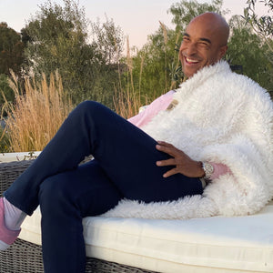 A smiling man on a couch outdoors, trees in background, BIG LOViE Big Guardian Angel Blanket in Whisper White on his shoulder