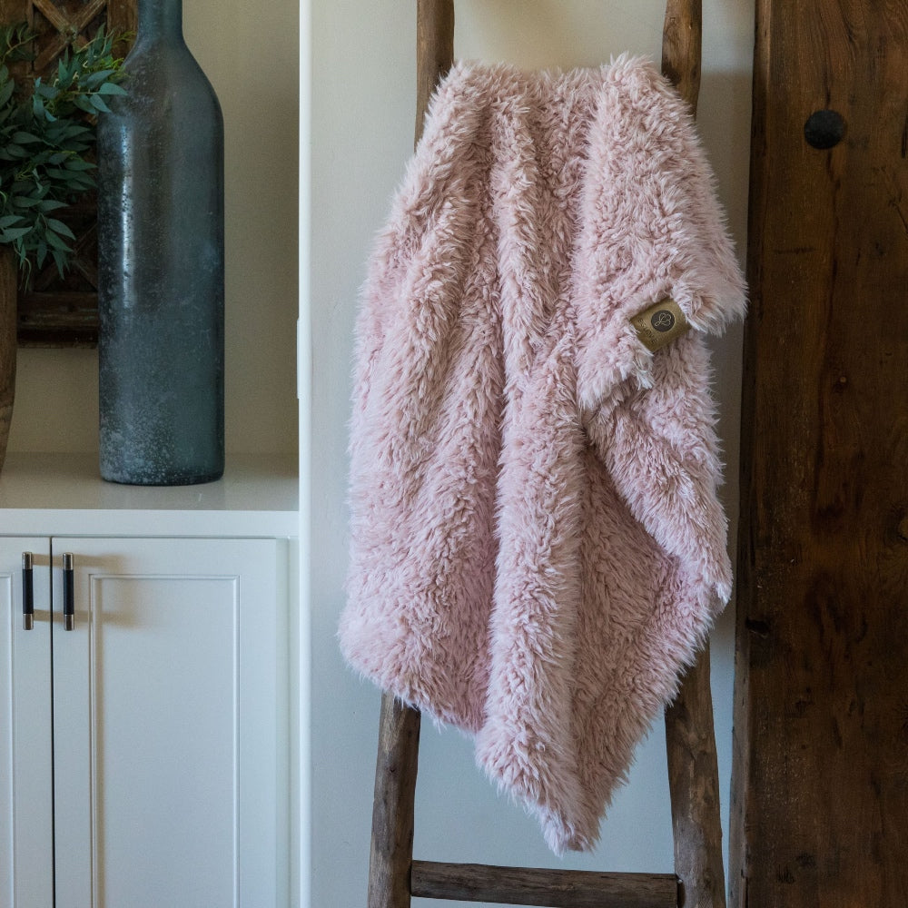 Little Guardian Angel blanket in Dusty Pink, llama fabric, on a wooden ladder in front of white cabinets