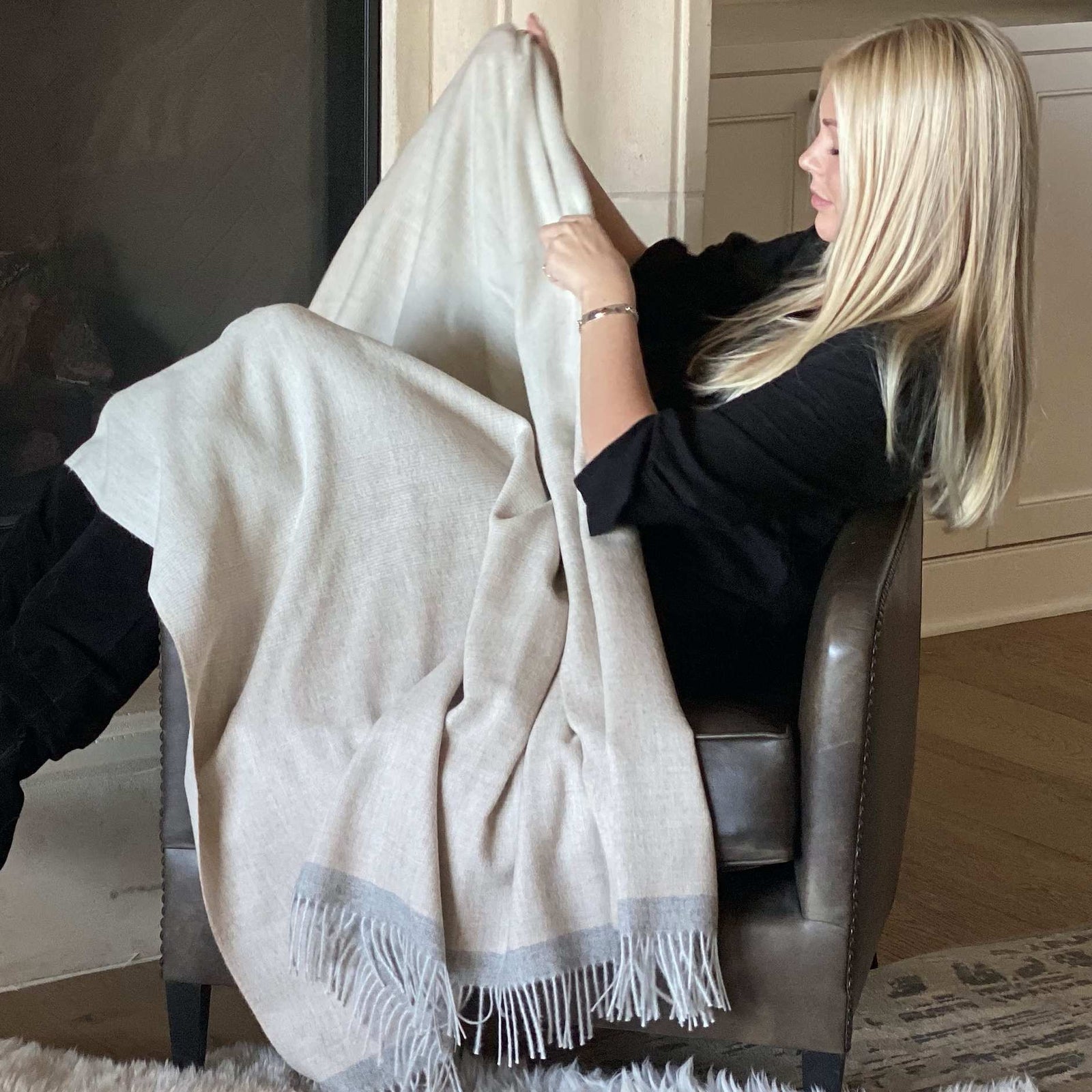 Woman snuggling into a chair with a BIG LOViE Soul Coco 100 percent baby alpaca blanket.